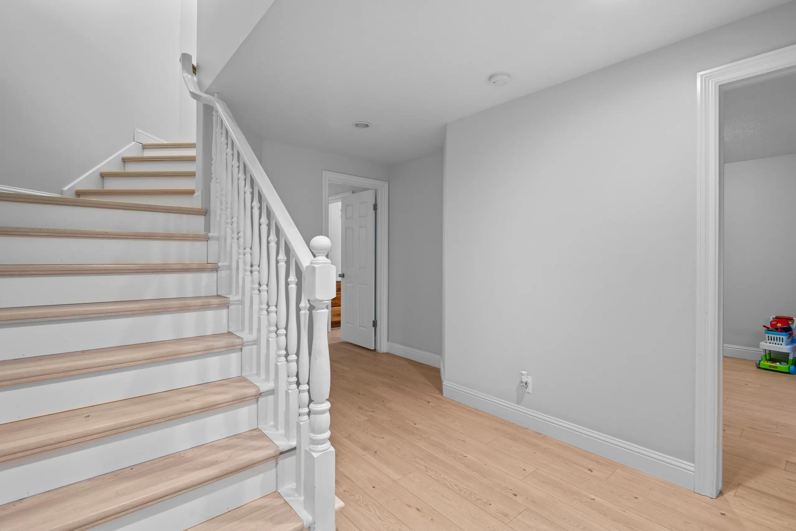 Finished basement stairway with oak treads, a white painted railing and wide-plank flooring across the landing