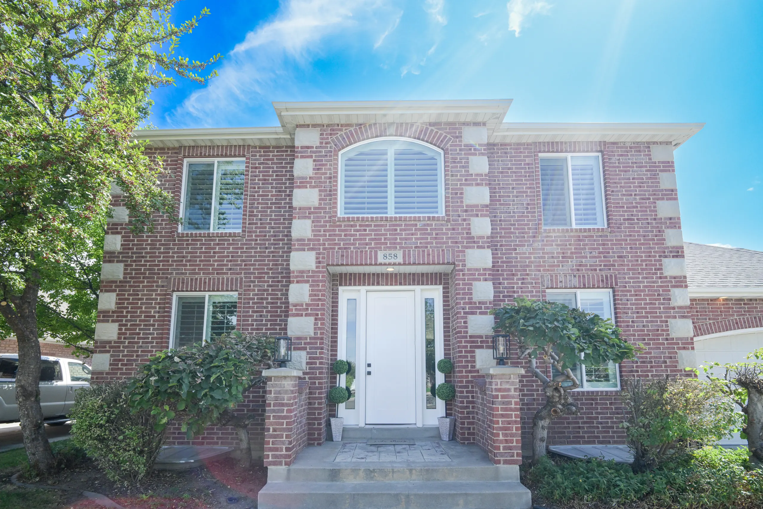 Front entry of a Layton brick home with an arched transom window above the door, white trim stone and clipped topiaries either side of the steps