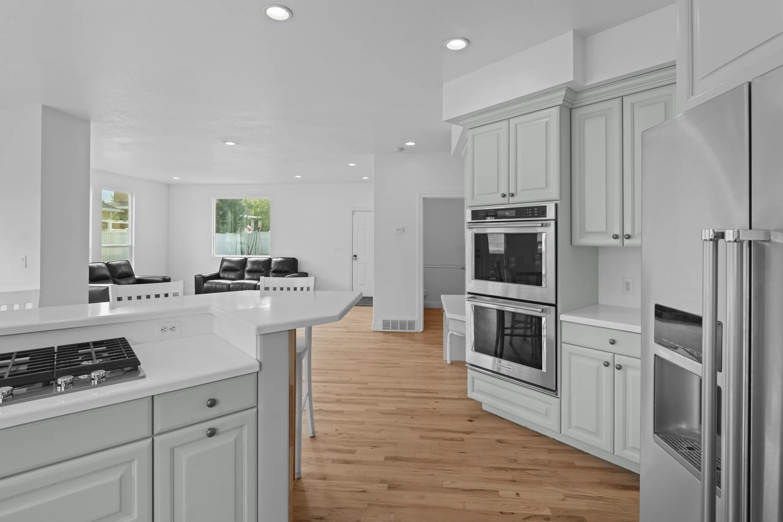 Kitchen with a quartz breakfast bar, gas cooktop, stainless double wall ovens and pale cabinetry, open through to the family room