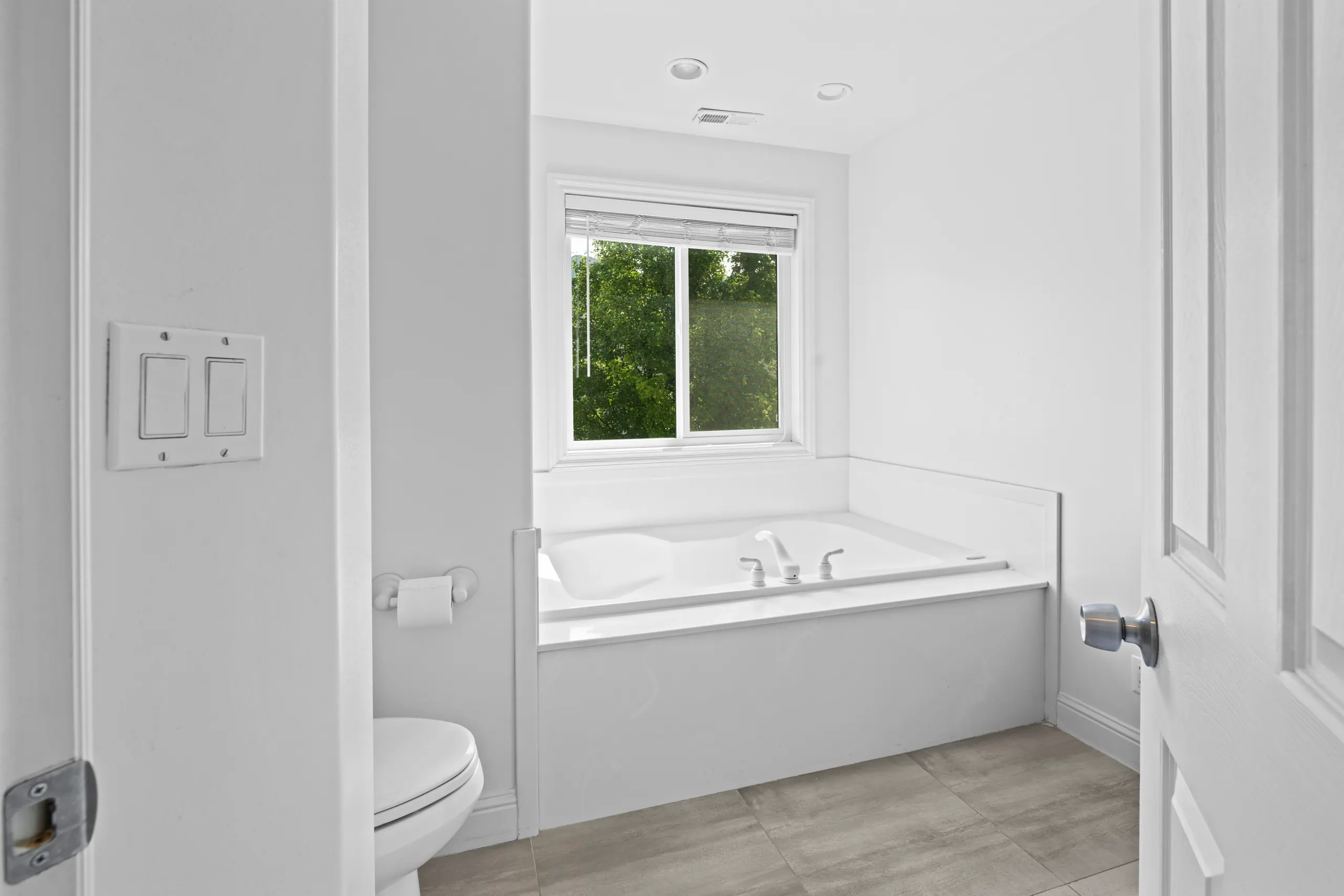 Primary bathroom with a drop-in soaking tub beneath a garden window and grey tile flooring